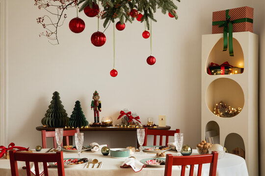 Christmas dining room with red chairs, decorated table, and hanging evergreen branches with red ornaments.