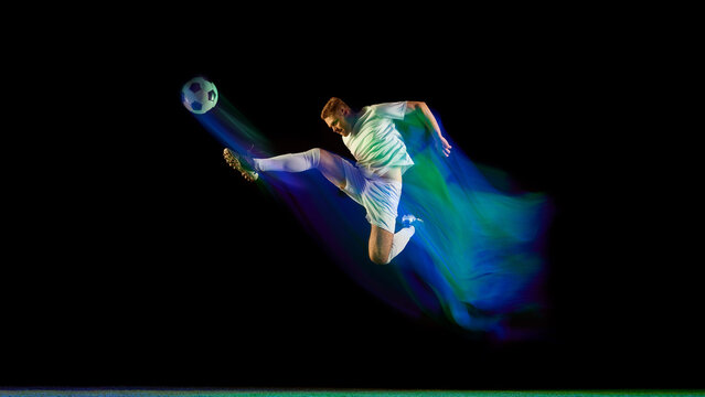 Soccer player performing midair kick surrounded by glowing blue and green light motion. Concept of ambition, focus, and physical excellence used in sports branding and visual campaigns.