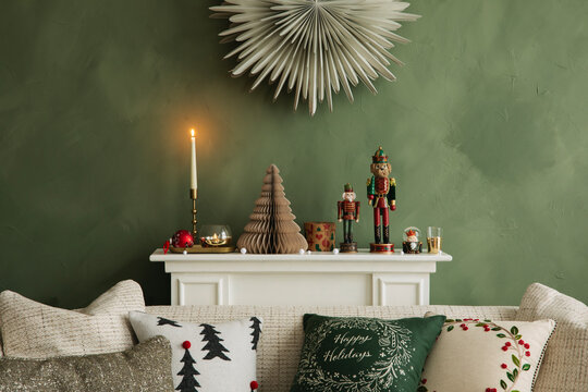 Christmas mantel styling with candles, nutcrackers, and festive ornaments on a green wall above a cozy sofa.