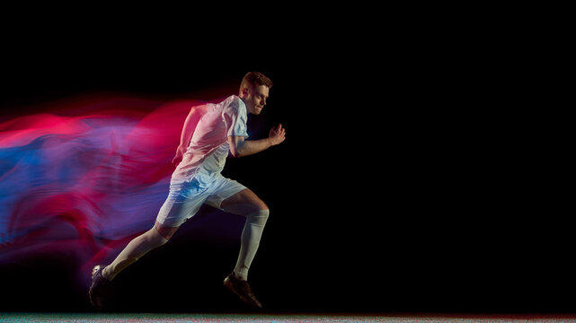Football player running fast with glowing red and blue motion blur in dynamic action. Concept of endurance, focus, movement used in athlete training, advertising, and sports analytics.