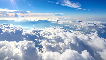 Fluffy clouds sprawl under a clear blue sky, sun glaring in distance, creating a bright, airy, and celestial atmosphere