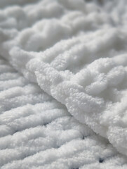 close up of a soft white chunky knitted blanket texture and fold with shallow depth of field