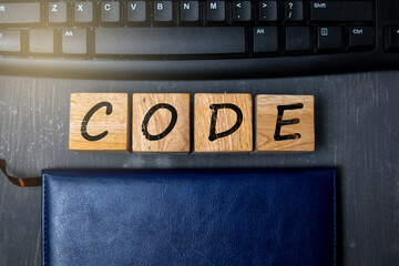Wooden blocks with the word CODE placed on a keyboard and notebook background, symbolizing programming, software development, and modern digital technology concepts.