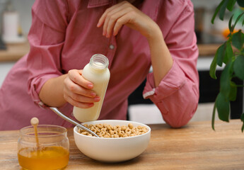 Woman female hands prepare a quick breakfast of dry round corn flakes balls, honey milk on a kitchen