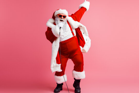Santa performs on stage in a red suit with white fur singing into a microphone against a pink background creating a fun festive moment for holiday lovers