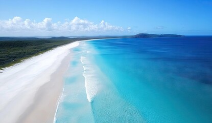 An aerial view of a pristine white sandy beach with turquoise ocean waves and green hills in the distance