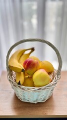 Wicker basket with fresh bananas and apples on wooden table in soft natural light.