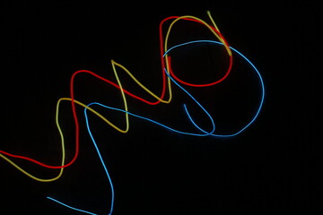 Abstract composition with glowing EL wire coils and colorful scribbled light trails (red, yellow, blue) on a black background.