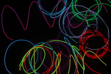 A chaotic, energetic scribble of multiple glowing EL wire lines in various colors, creating a vibrant abstract pattern on a black background.