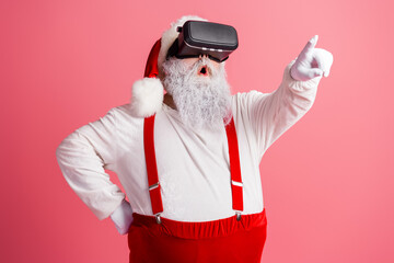 Santa in a VR headset points forward in pink studio wear suspenders white costume festive workshop...