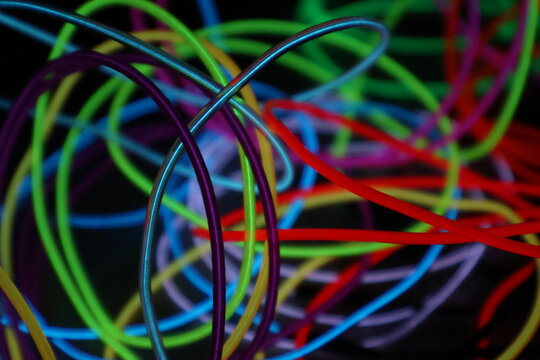 A chaotic, energetic scribble of multiple glowing EL wire lines in various colors, creating a vibrant abstract pattern on a black background.