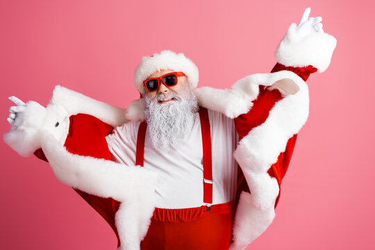 Santa in red suit with pink background dancing and posing for a festive photo wearing fur trim and glasses