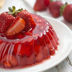 A close up view of a strawberry gelatin dessert with fresh strawberries on a white plate surface