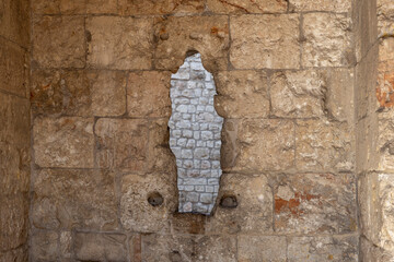 A textured close-up of an old stone wall with a unique, vertical, irregular-shaped hole revealing an inner layer of smaller, rougher stones.