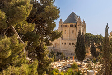 jerusalem, Israel, 2 November 2025,  A scenic view of the Church of the Dormition on mount zion, partially framed by lush green pine trees, overlooking a cemetery in the foreground.