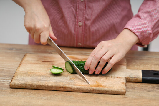 Female hands cutting a cucumber on a wooden board on the table