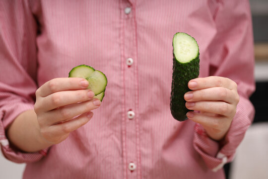 Female hands holding a sliced cucumber and slices, wearing a red shirt. Demonstration of slicing