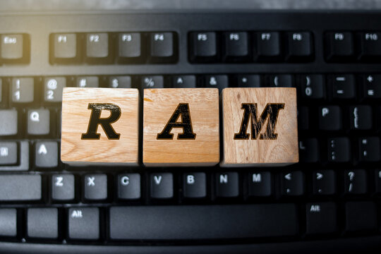 A conceptual photo showing wooden blocks spelling “RAM” placed on a desk near a computer keyboard, symbolizing memory, data processing, and computer performance in modern technology.
