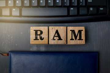 A conceptual photo showing wooden blocks spelling “RAM” placed on a desk near a computer keyboard, symbolizing memory, data processing, and computer performance in modern technology.