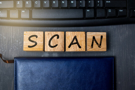 Wooden blocks spelling “SCAN” placed near a keyboard and notebook, representing digital scanning, data processing, and modern technology concepts in an organized workspace setting.