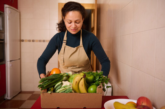 Woman In Apron Packs Fresh Produce Box In Kitchen For Groceries And Home Cooking