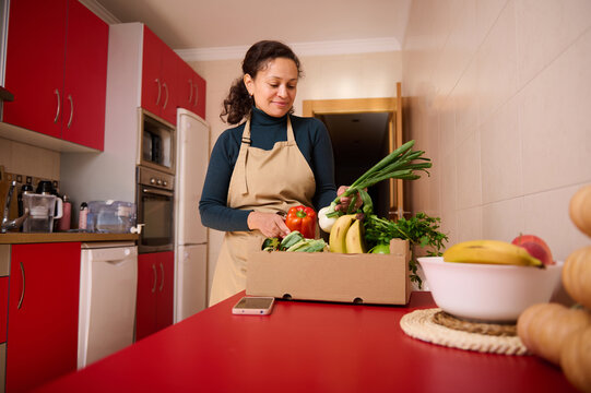 Woman In Apron Unpacks Fresh Groceries In A Red Kitchen For Healthy Home Cooking