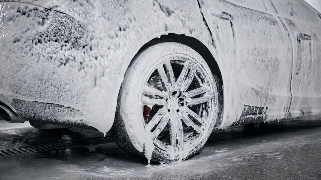 Close-up of car wheel covered with foam during detailed cleaning. Concept of car care cleaning products, service marketing, road safety awareness.