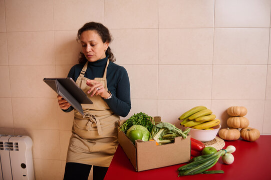 Vendor Reviewing Tablet in Kitchen Studio Surrounded by Fresh Produce - Powered by Adobe