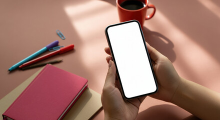 Person holding a smartphone with a blank screen at a workspace