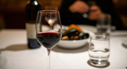 A glass of red wine on a dining table with a blurred background of a person and food