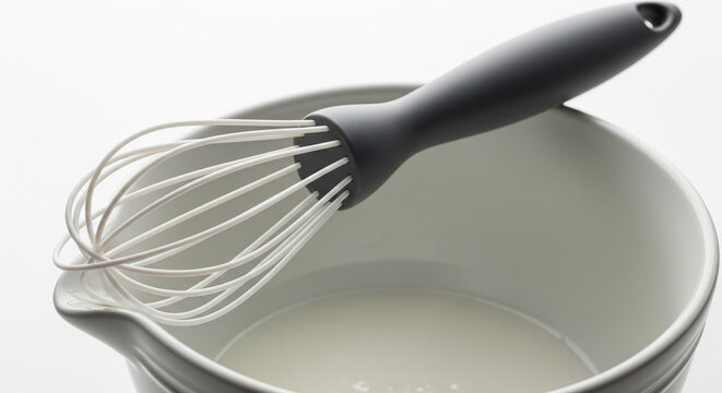 Silicone Whisk Resting in a Bowl of Creamy Liquid for Baking.
A clean, high-angle close-up shot capturing a modern kitchen moment. A sleek silicone or plastic whisk with a dark grey handle