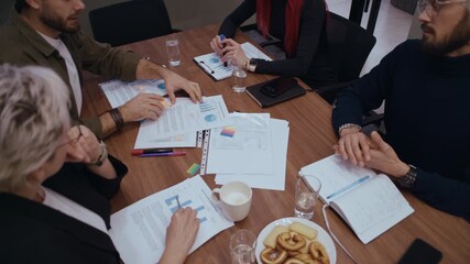 Professional office environment showing teamwork as four coworkers review financial performance charts and documents. One employee points and marks key data while colleagues follow and discuss insight - Powered by Adobe