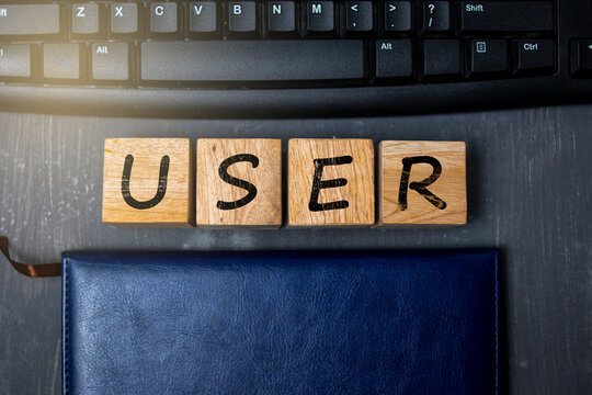 Wooden blocks spelling the word “USER” placed beside a keyboard and notebook, symbolizing digital identity, technology access, user interface, and modern online interaction in tech environments.