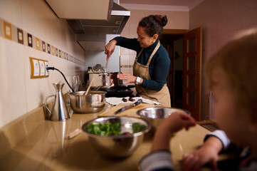 Busy Home Kitchen With Woman Cooking And Child Watching In Warm Evening Light