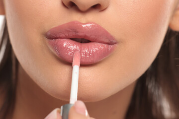 Close-up of a woman applying pink lip gloss, studio shot on a white background