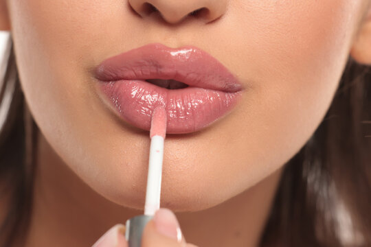 Close-up of a woman applying pink lip gloss, studio shot on a white background - Powered by Adobe