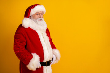 Santa in red suit with white fur trim stands against a bright yellow background ready for the holiday season