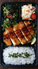 Overhead shot of Japanese chicken katsu bento box with rice, salad, and coleslaw in black container on wooden surface