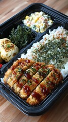 Bento box with tonkatsu rice seaweed salad and egg rolls overhead shot on wooden table in natural light