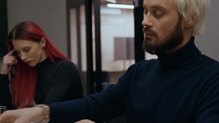 Businessman wearing a watch finishes writing in his notebook using a pen, then takes off his glasses and rubs his face, beard, and neck with visible tiredness - Powered by Adobe