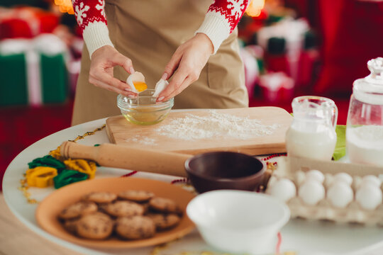 Festive kitchen scene of a person cracking an egg and preparing dough for cookies during Christmas season with flour milk rolling pin and baking tools around bright decorations