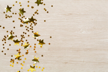 Golden star shape confetti on wooden background, top view