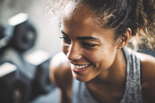 A smiling woman exercises in a gym, showcasing determination and fitness, with weights visible in the background.