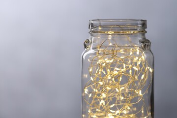 Christmas lantern. Glowing fairy lights in glass jar against grey background, closeup. Space for text