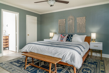 Modern boho bedroom interior. Bed, pillows, macrame, wood bench, rug.