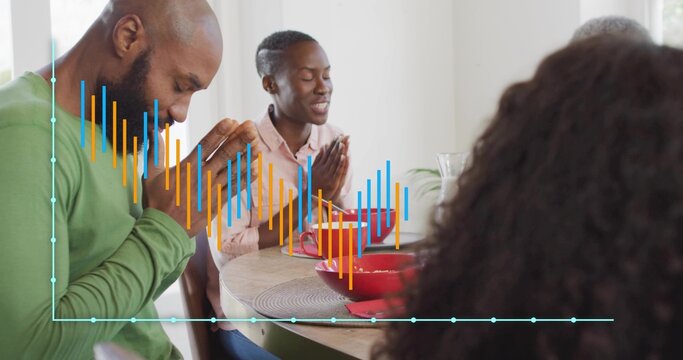 Praying family in green and pink at round wooden table at home, red bowls, chart overlay