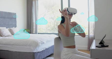 Sitting woman wearing white VR headset crop top pants using teal cloud overlays in bedroom