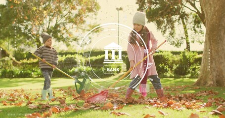 Raking siblings wearing knit hats collecting fallen leaves on sunlit lawn at park, with red rake