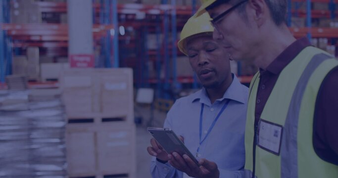 Fototapeta Holding tablet, two workers inspecting inventory in aisle, wearing hard hats and hi-vis vest