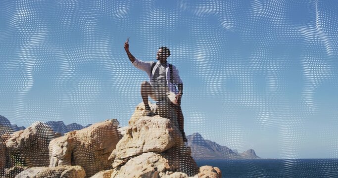 Taking hiker wearing shorts and hiking shoes holding phone high on rocky coast, with backpack
